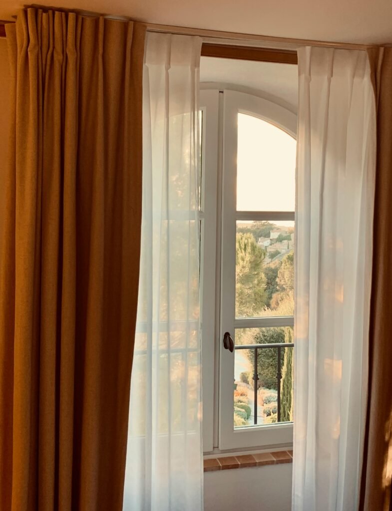 Warm sunlight through curtains reveals a scenic view of Cassis, France.
